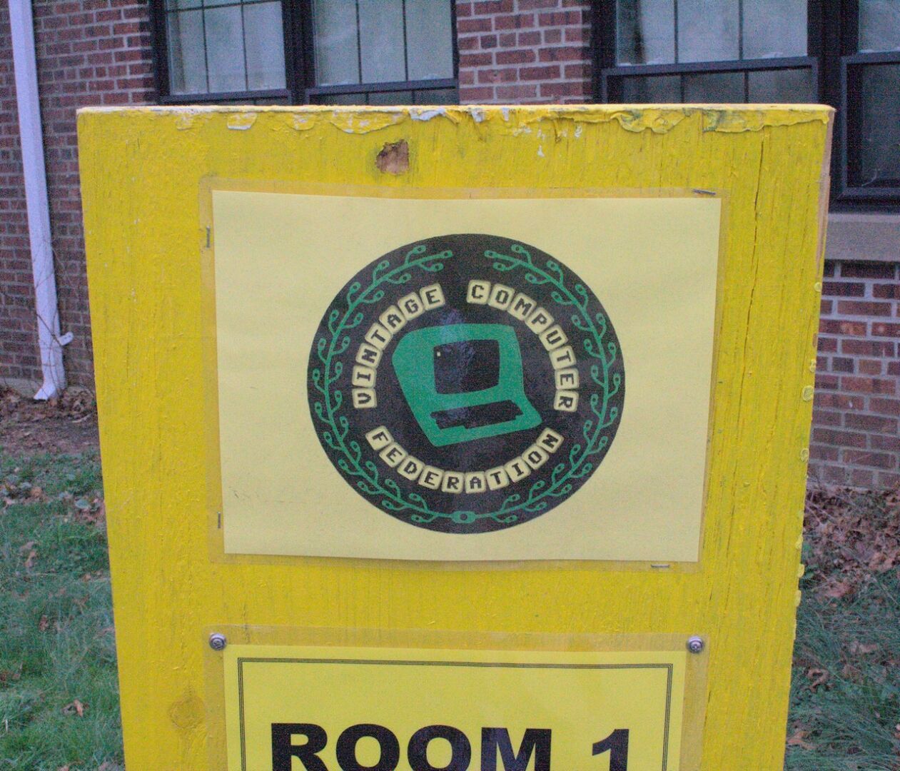 The Vintage Computer Federation logo, which features an older-style computer in the middle of a circle, placed onto a wooden sign.