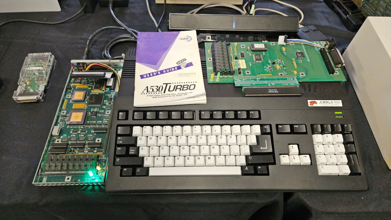 An Amiga 500 computer with an open device attached to the left side, and another circuit board sitting on top of the computer.